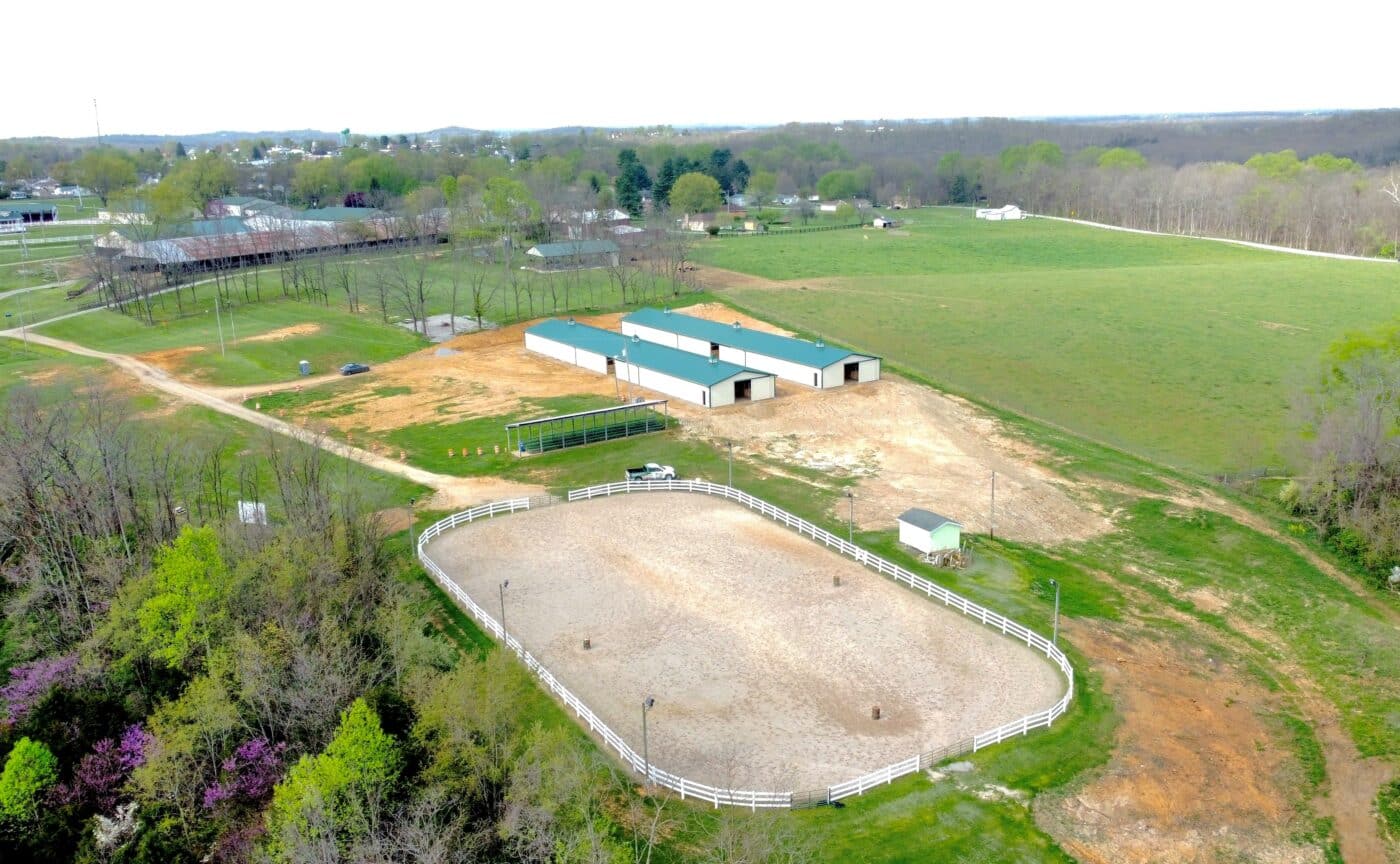 aerial view of two cream and green metal roof 38x64 equestrian pole barns with outdoor horse ring