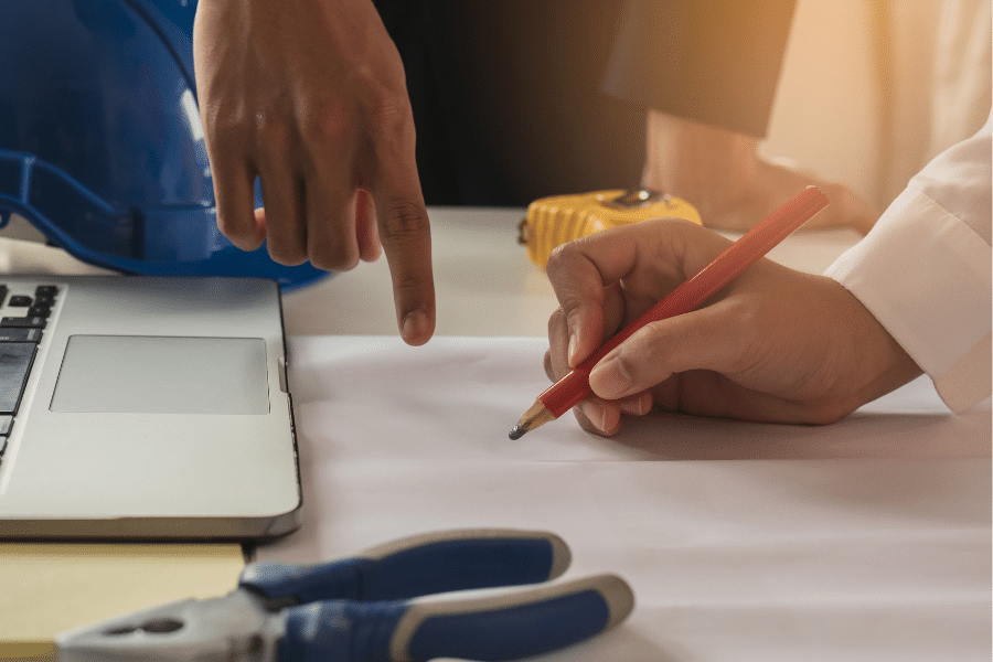 two people planning the design of their 70x100 pole barn garage one pointing to a piece of paper and the other beginning to draw with a red pencil