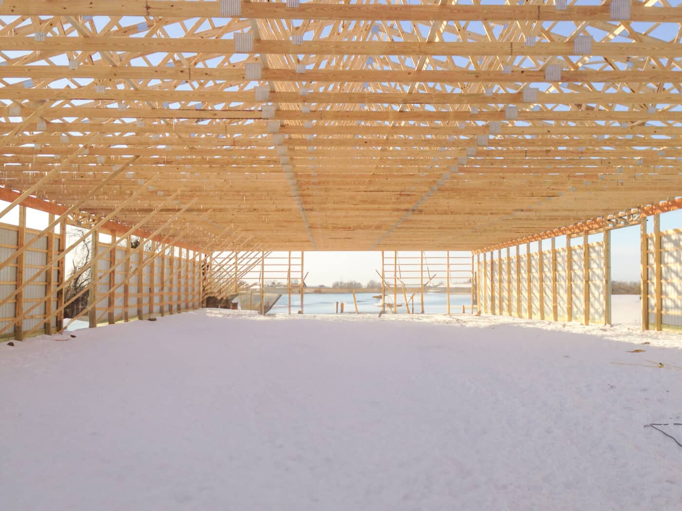 view of wooden roof trusses placed to create roof on frame of pole barn from the interior of the frame