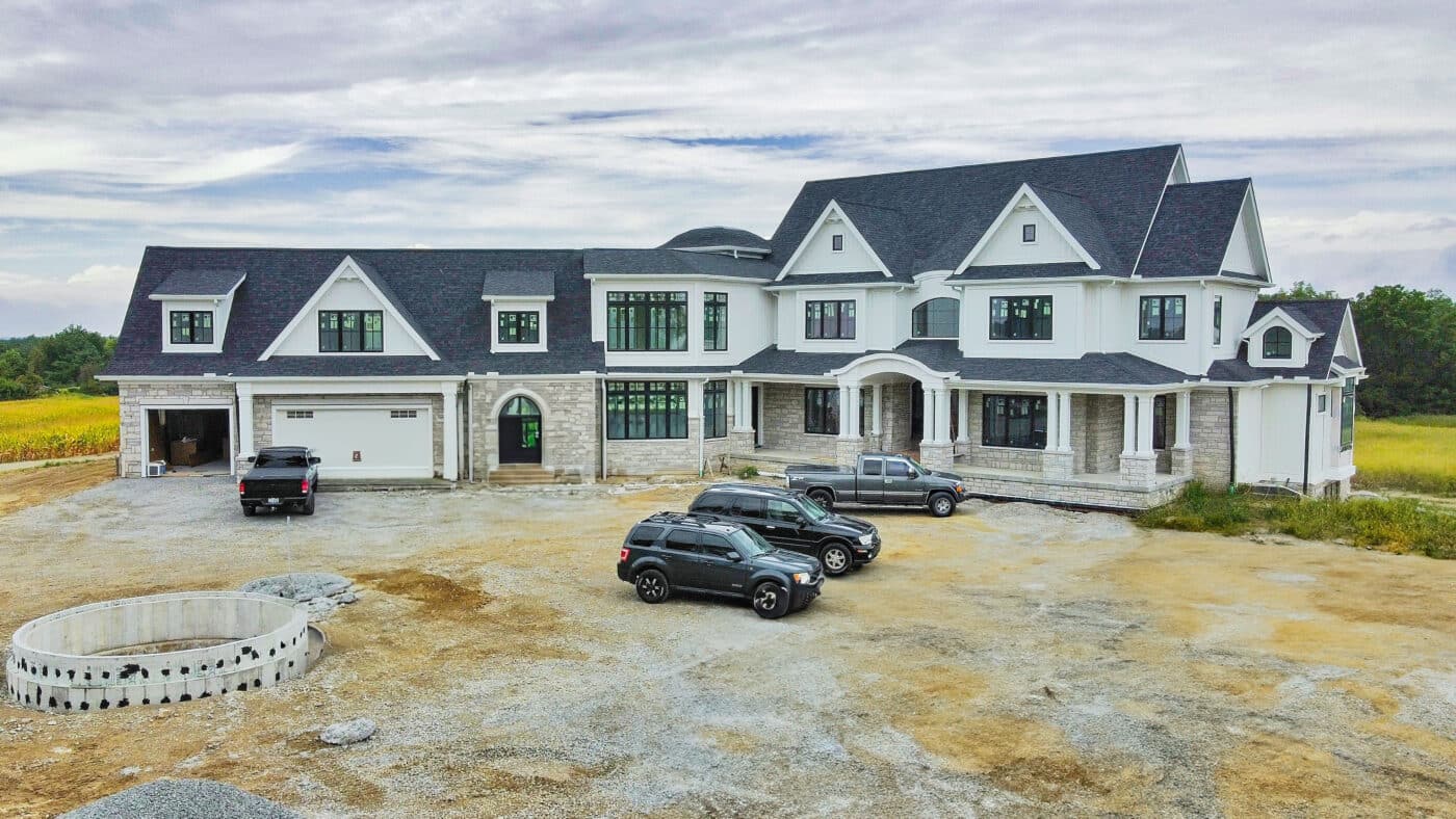 white 50x100 barndominium with stone deatailing on 1st story and attached garage with multiple cars parked in front of it