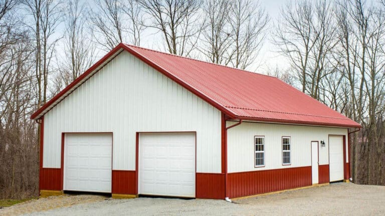 white and red 50x100 metal pole barn garage with red metal trim and roof featuring two white overhead doors on front and a side door and overhead door on the side alongside two windows