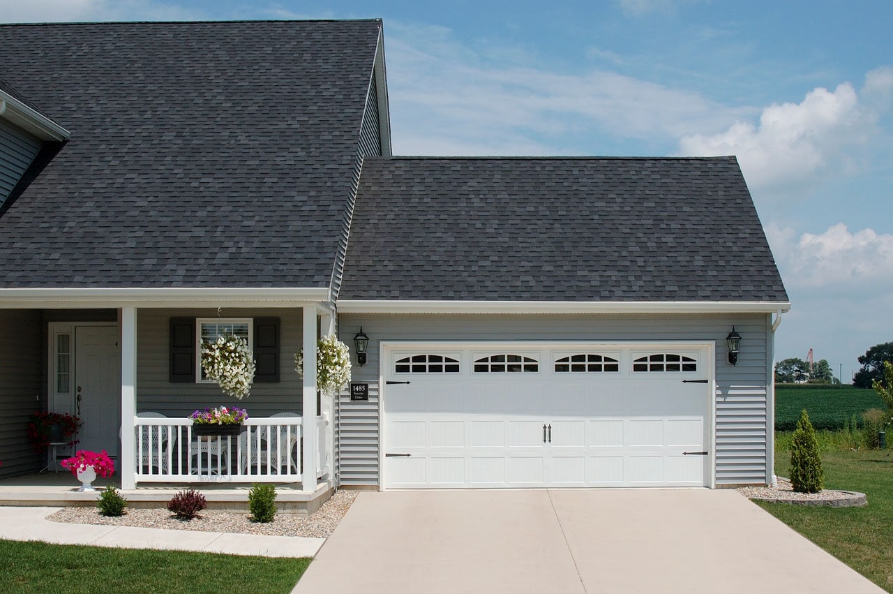 white CHI garage door with transom windows on light gray house with shingle roofing and a front porch