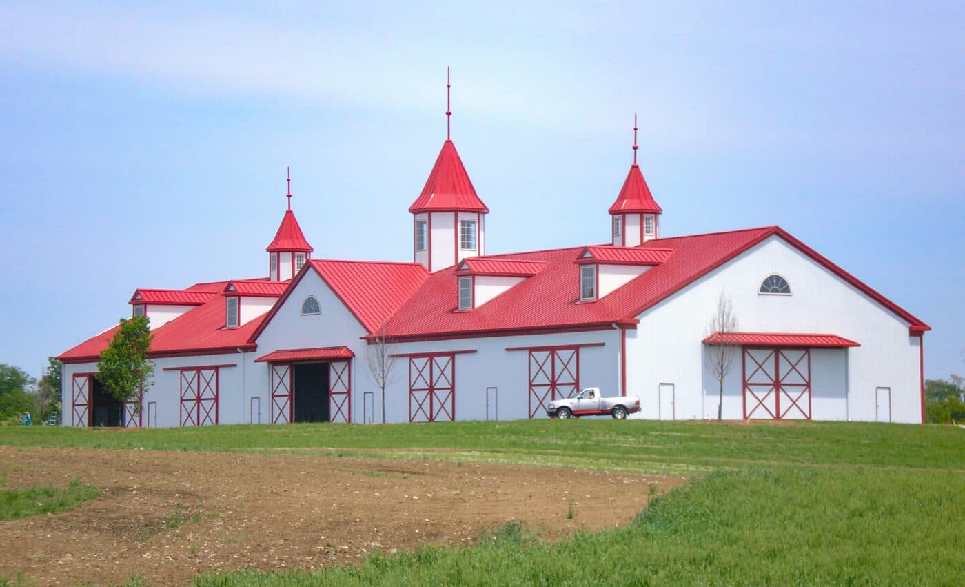 white agricultural pole barn kits in Independence kY with red trim and a red metal roof featuring three metal towers and 4 window bays on top