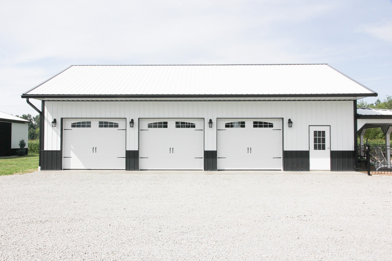 white and black metal pole barn garage with three white overhead doors with transom windows