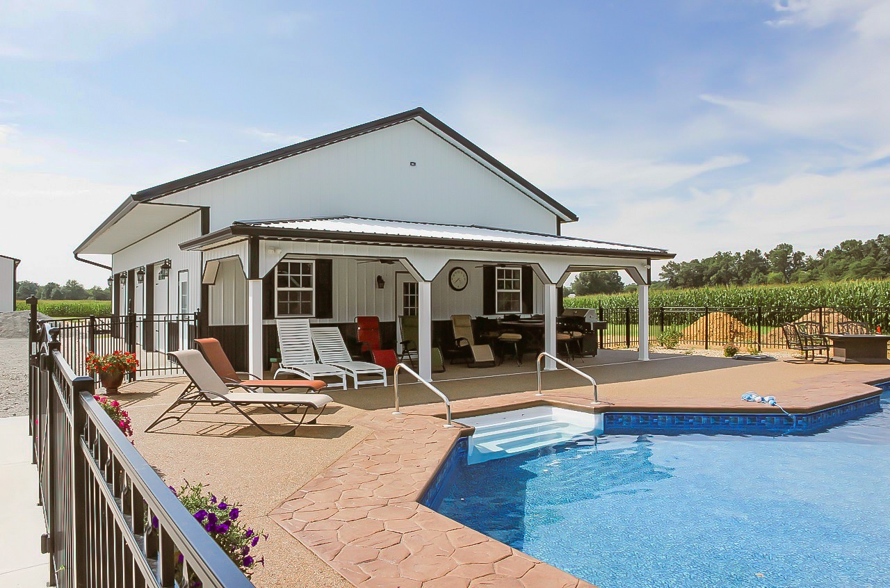 white and black pole barn garage with porch overlooking a pool
