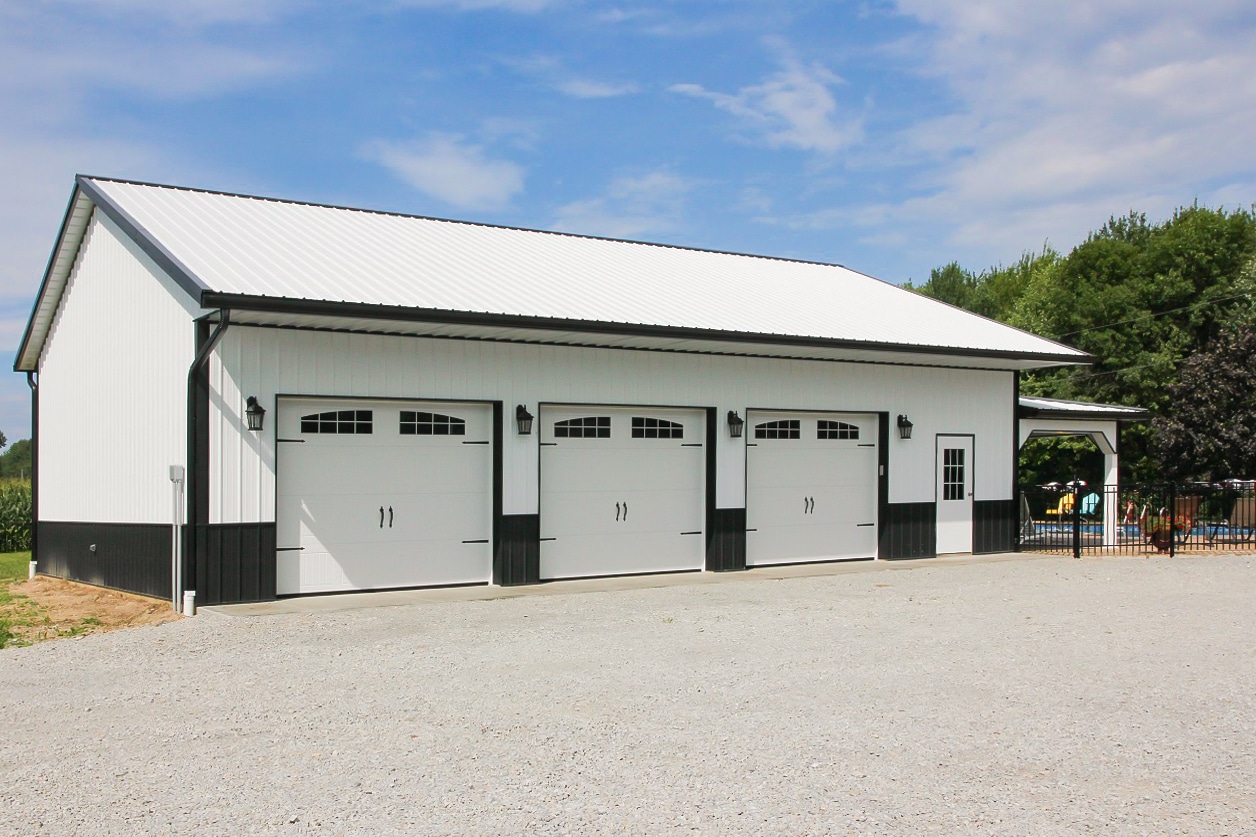 white and black three car 30x33 pole barn garage being used as a pool side storage space
