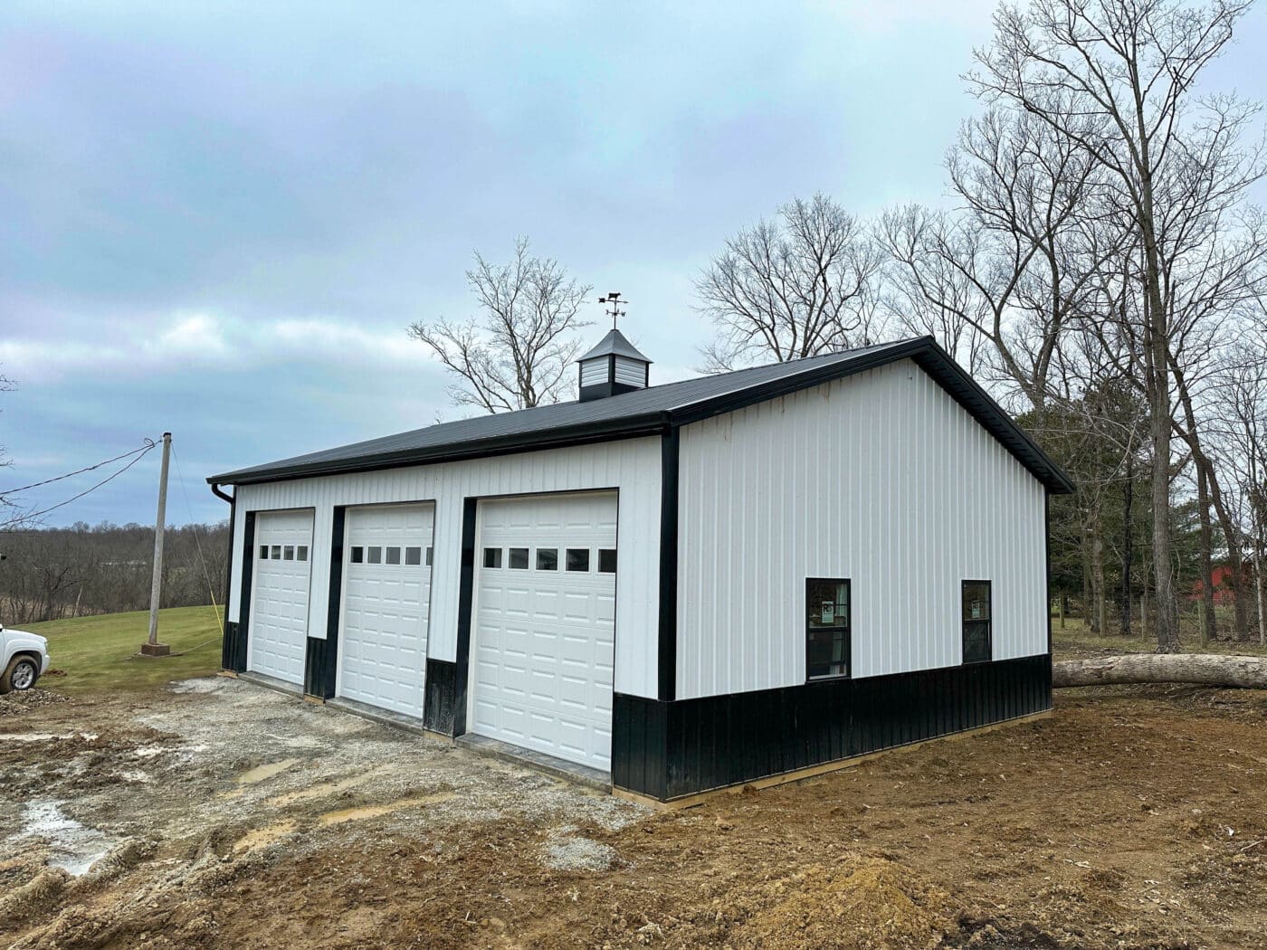 white and black trimmed 30x40 pole barn garage built by dutch builders with three overhead doors with transom windows