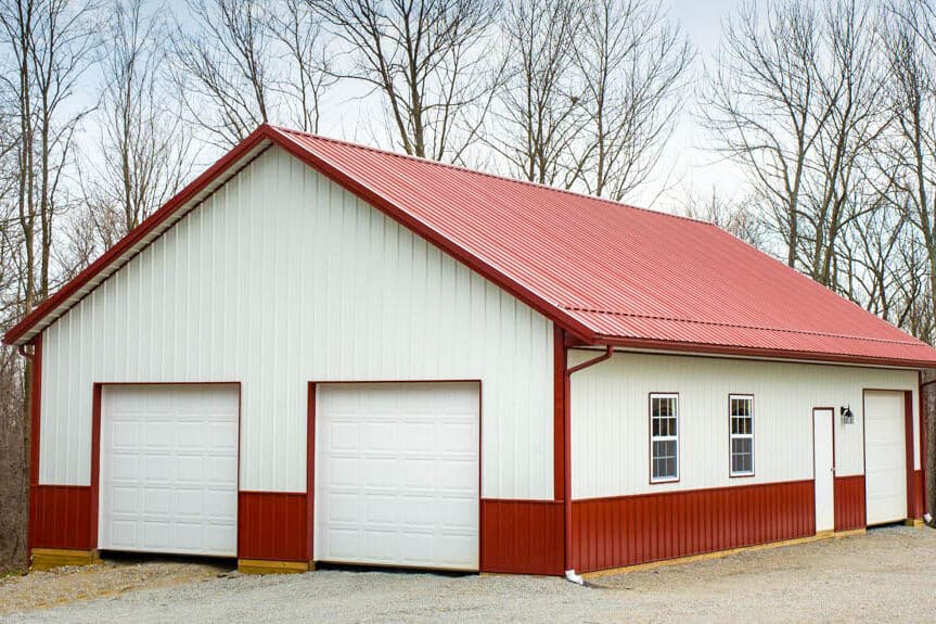 white and red metal pole barn garage with red metal trim and roof featuring two white overhead doors on front and a side door and overhead door on the side alongside two windows