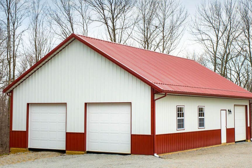 white and red trimmed two car pole barn garage with red metal roof and two white overhead doors