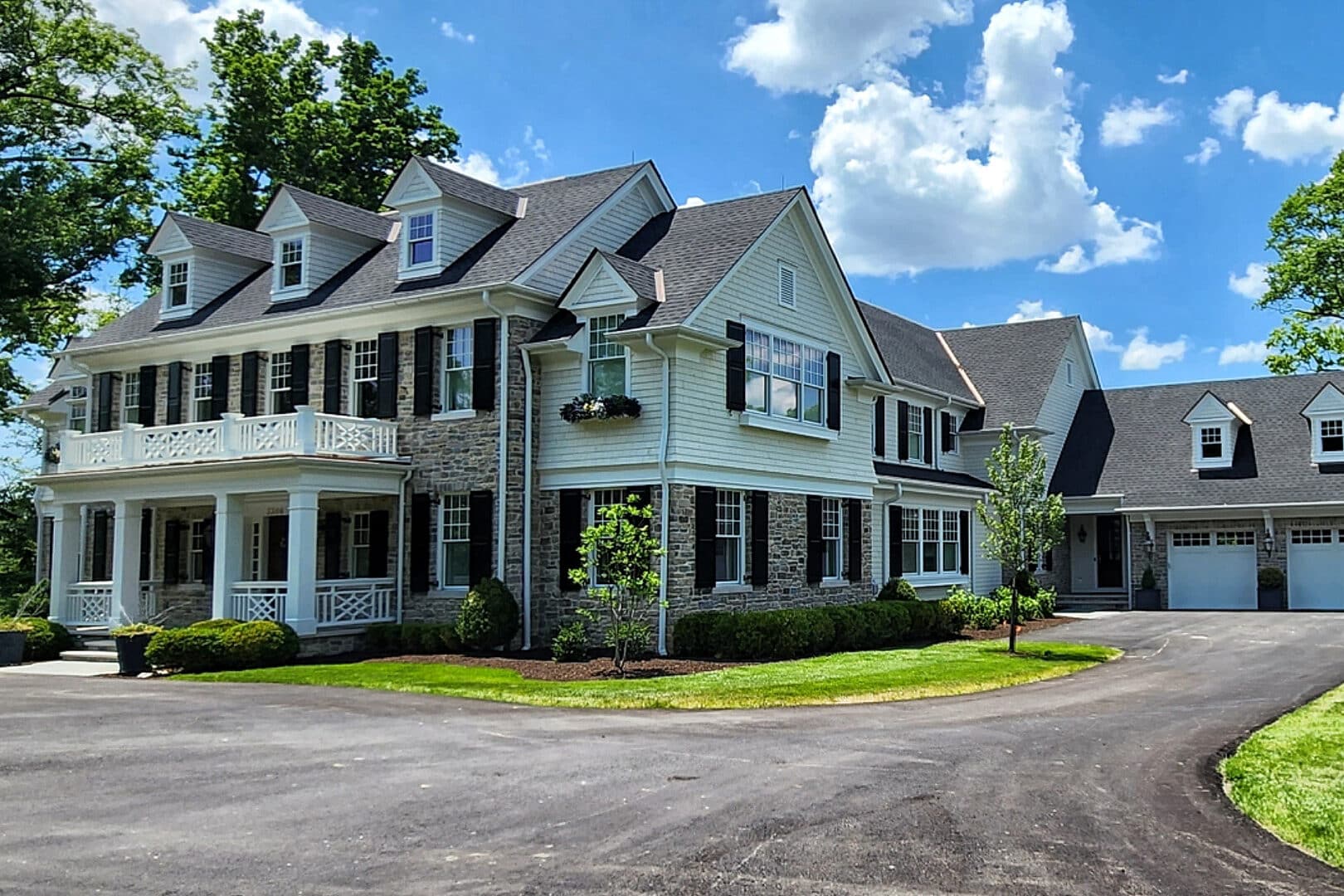 white and stone sided two story barndominium with a front porch and top balcony featuring an attached three car garage with three white overhead doors with transom windows