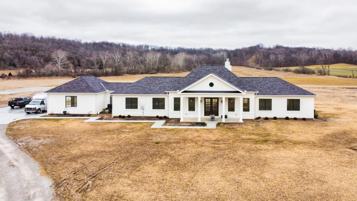 white barndominium with shingle roof and long driveway