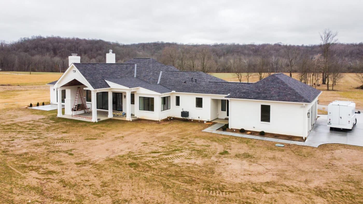 white barndominium with shingle roof multiple windows and front porch