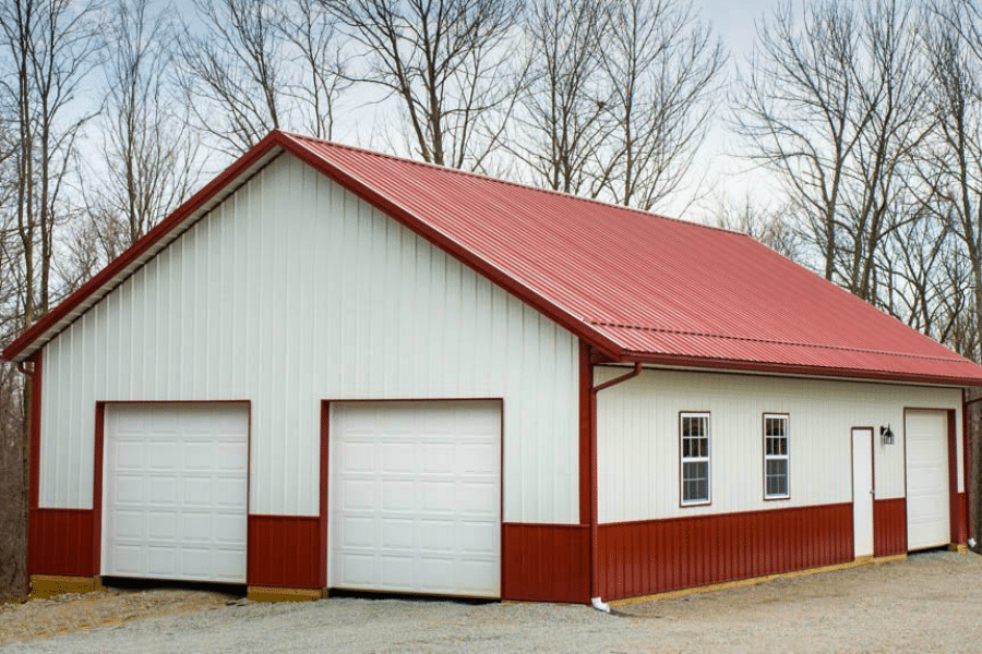 white metal sided and red trimmed two car pole barn garage with red metal roof two white overhead doors and red metal paneling along the bottom