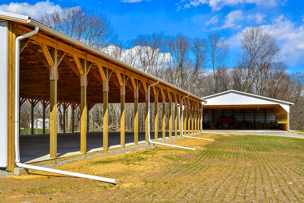 white sided agricultural pole barn with openings storing hay and equipment