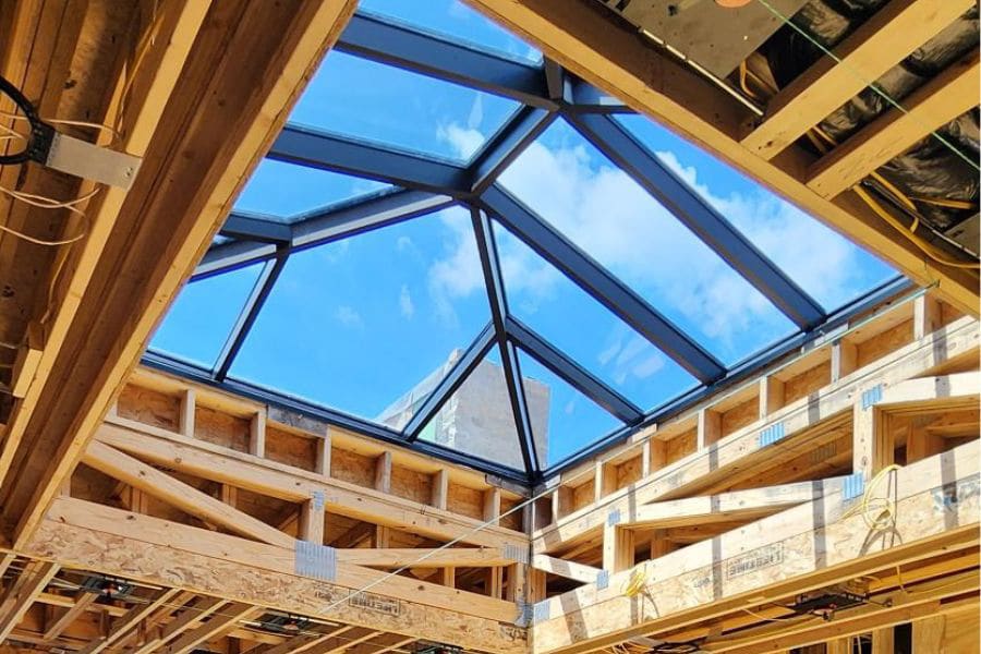 wooden roof trusses around skylight with view of clear blue sky